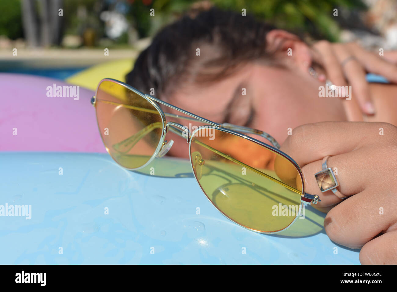 Junge Frau schlafend 7 Sonnenbaden auf eine lilo in einem Schwimmbad. Metall gelb Sonnenbrille im Vordergrund eingerahmt. Sommer vibes, Freizeit, Spaß und Freizeit Stockfoto