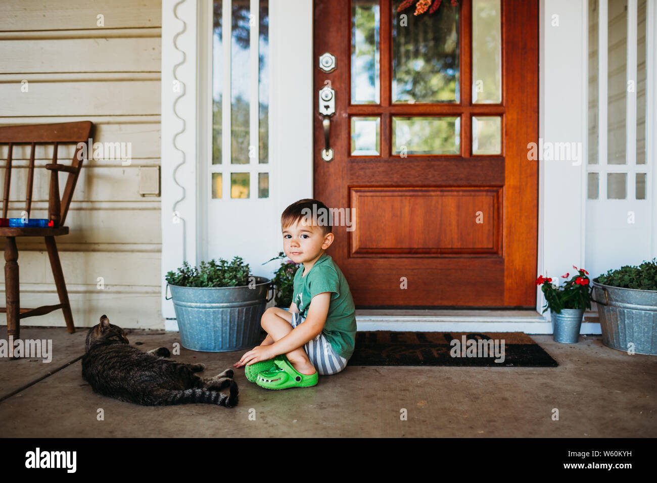 Junge Junge sitzt vor der Eingangstür mit Haustier Katze Stockfoto