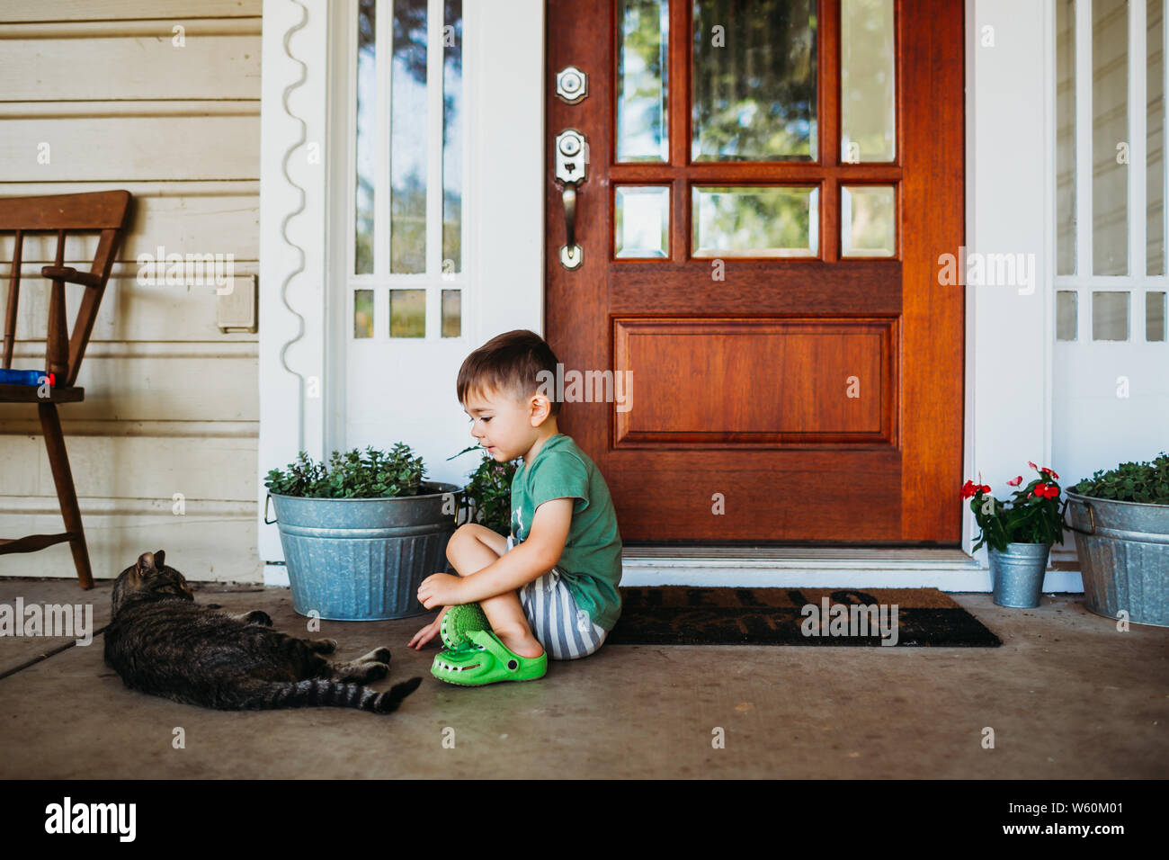 Junge Junge sitzt vor der Eingangstür petting kurze Haare Katze Stockfoto