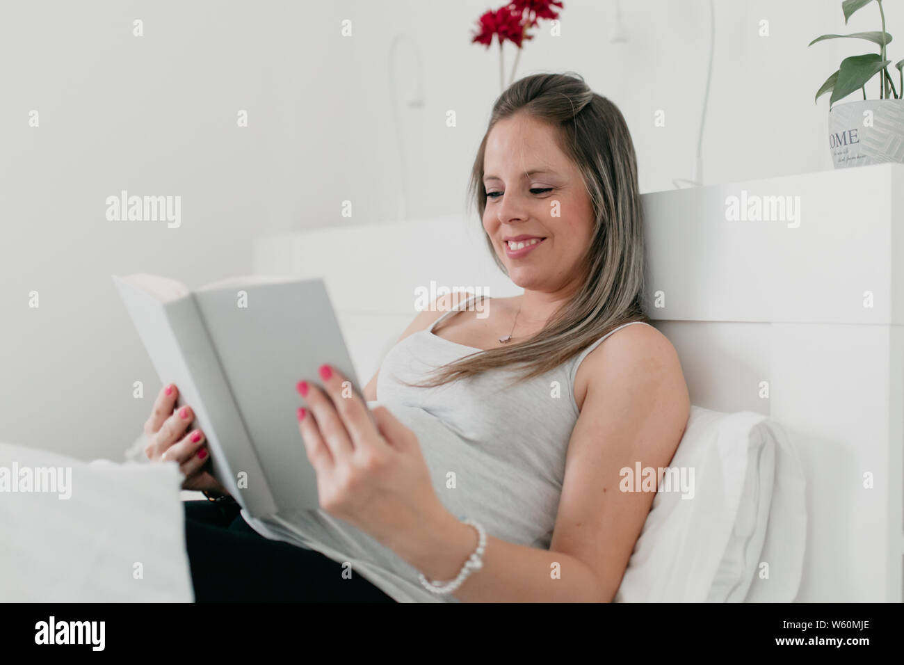 Schwangere blonde Frau im Bett liegen, ein Buch lesen Stockfoto