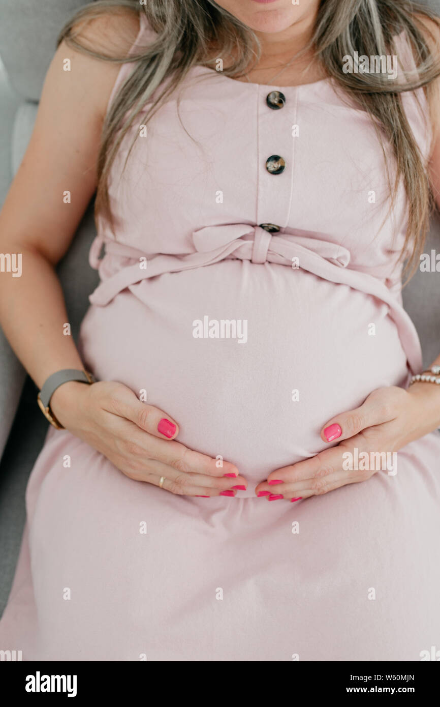Schwangere blonde Frau mit rosa Kleid berührt ihren Bauch an der Unterseite Stockfoto