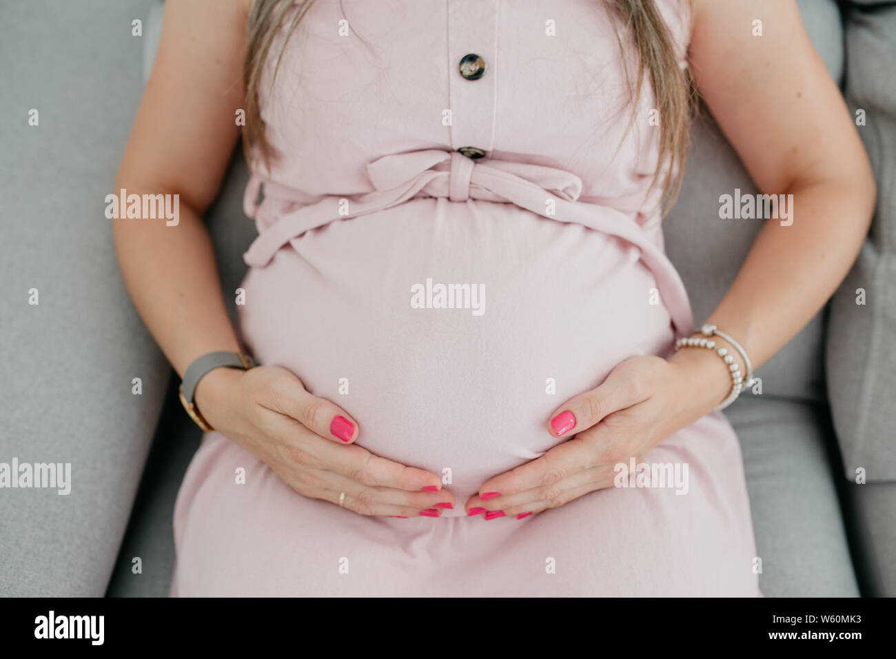 Schwangere Frau mit rosa Kleid berührt ihren Bauch an der Unterseite Stockfoto