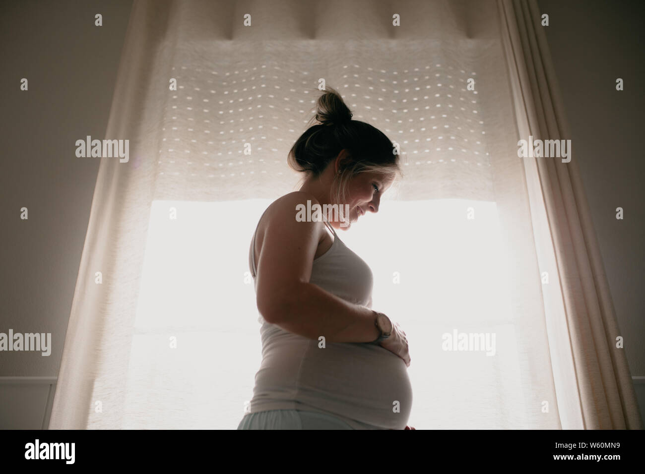 Hintergrundbeleuchtung der schwangeren Frau, ihren Bauch berühren. Stockfoto