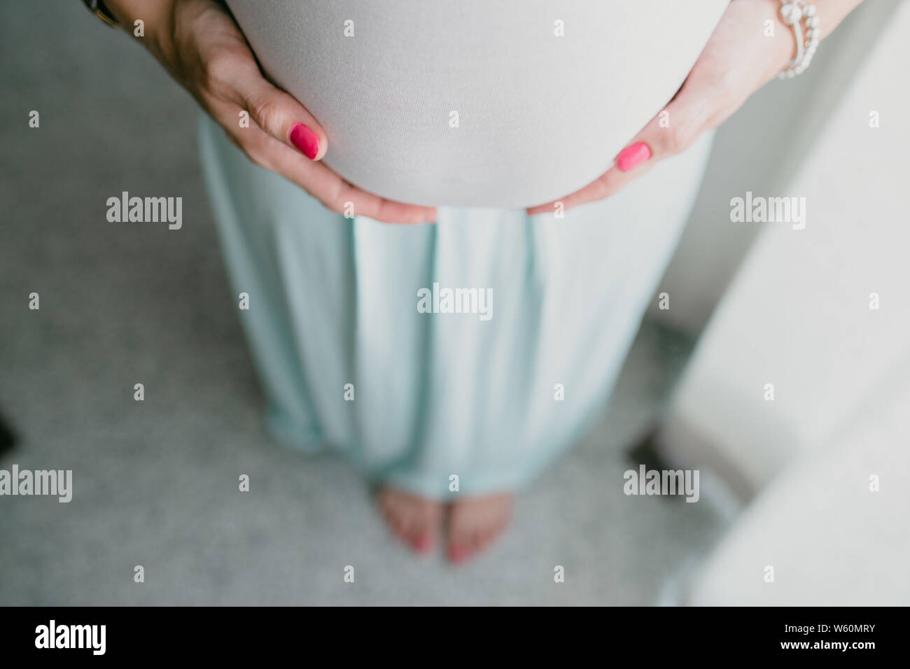 Bauch und Händen der schwangeren Frau, die im Hintergrund unscharf Füße Stockfoto