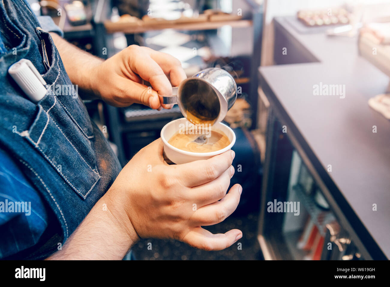 Nahaufnahme des Barista Hände, Cappuccino latte. Kellner server strömenden heißen Getränk in Kaffee Pappbecher. Kleine Unternehmen und Menschen bei der Arbeit. Stockfoto