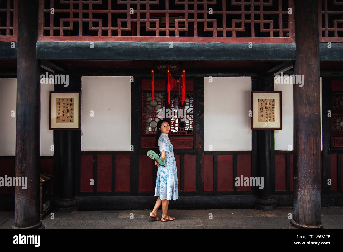 Asiatische Frau mit einem Handfächer in einem Tempel mit buddhistischen Sprüche geschrieben an der Wand in der chinesischen Stockfoto