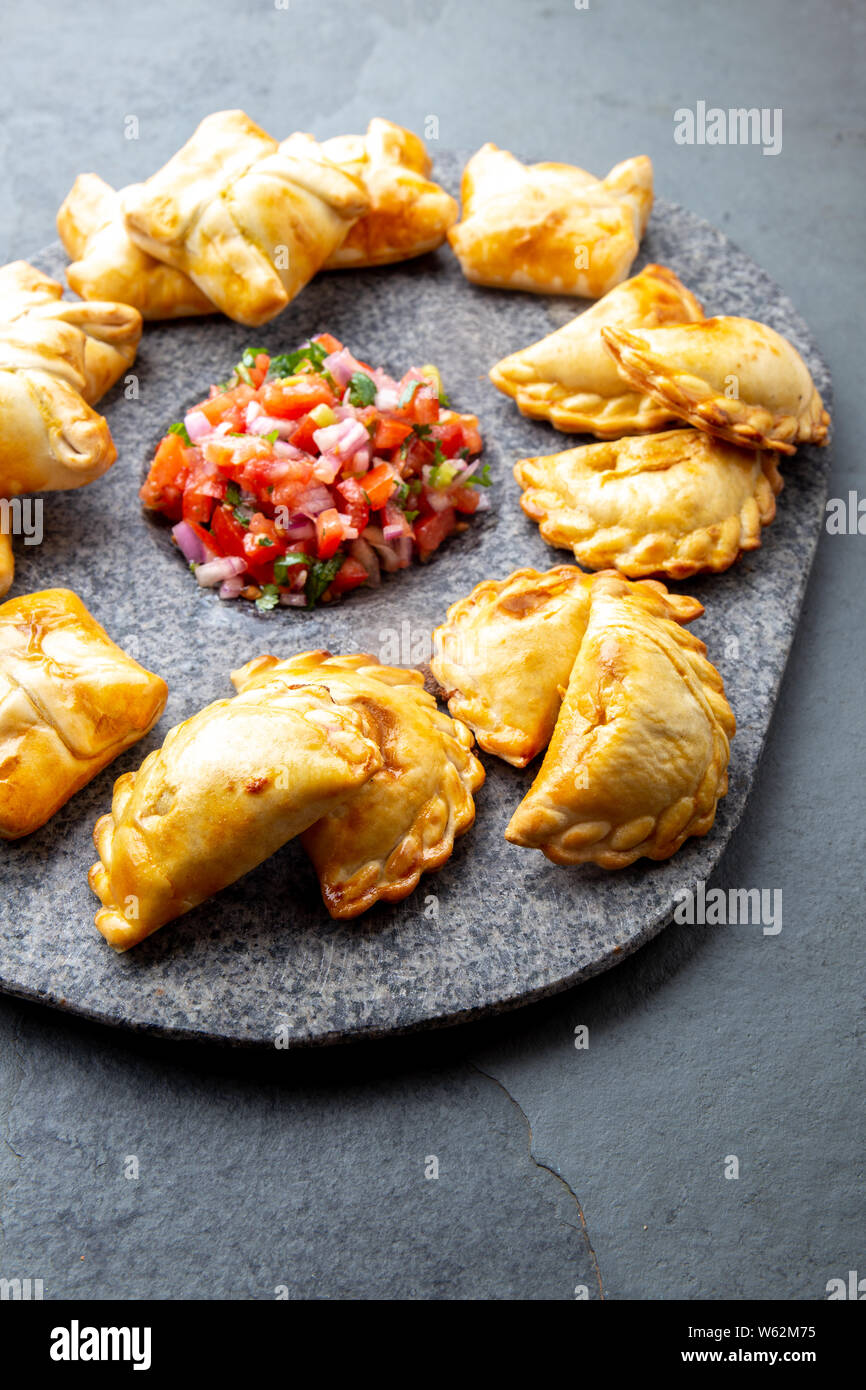 Verschiedene kleine Cocktail EMPANADAS auf der Steinplatte mit Tomatensauce und Guacamole. Grauer Hintergrund. Lateinamerikanische und Spanische typische Lebensmittel. Stockfoto