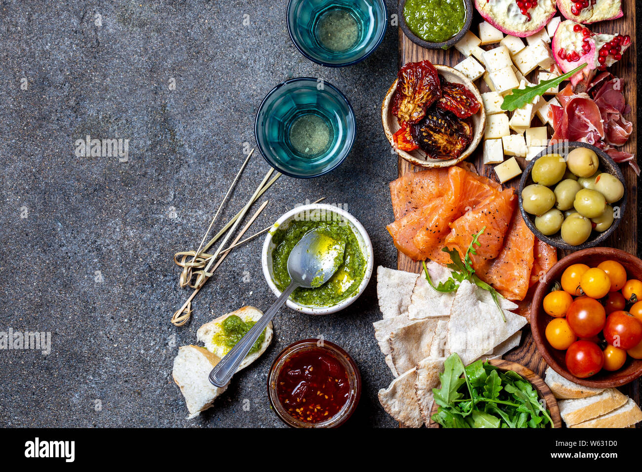 Antipasti. Wein Set Vorspeise. Schinken Serrano, geräucherten Lachs, getrocknete und frische Tomaten, Olivenöl, Käse, Wein an Bord. Ansicht von oben, grau cncrete Hintergrund. Stockfoto