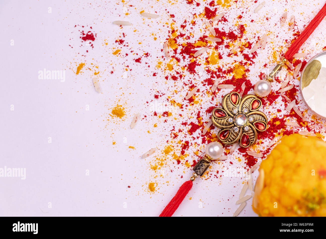 Raksha Bandhan Hintergrund mit einem Rakhi, verstreute Kumkum, Reiskörner, Haldi und Kardamom, Süßigkeiten auf weißem Hintergrund. Ein traditionelles rakhi die Ein Stockfoto