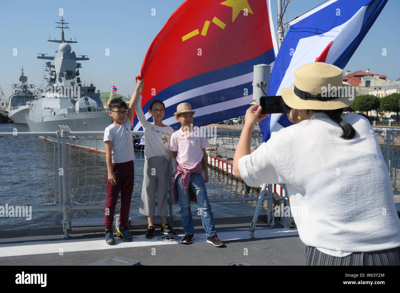 Chinesische Kinder holding Flags von China auf die Geführte-missile destroyer Xi'an der chinesischen Volksbefreiungsarmee Marine Oberfläche tritt am Ufer der Leutnant Schmidt in Sankt-Petersburg, Russland während der Vorbereitungen für die Russische Marine Parade Stockfoto