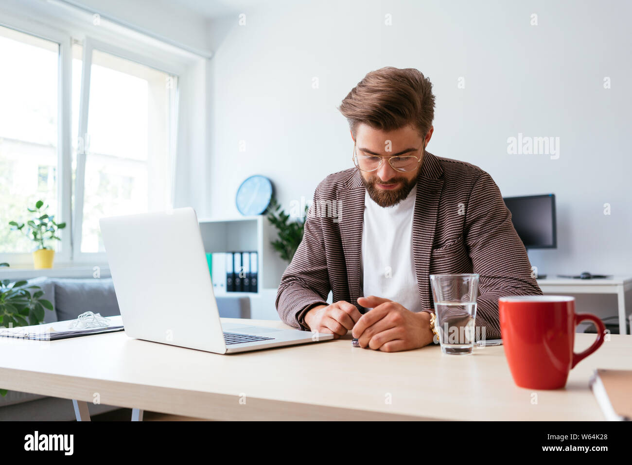 Mann mit Smartphone, während am Schreibtisch sitzt mit Laptop im Büro zu Hause Stockfoto
