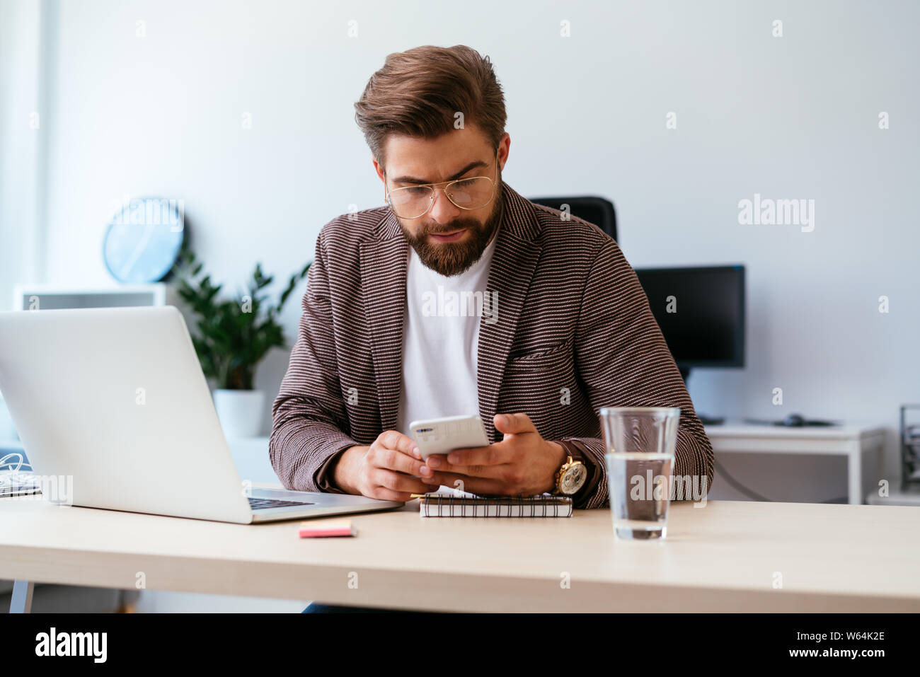 Junge Unternehmer prüfen Telefon während der Arbeit mit dem Laptop im Home Office Stockfoto