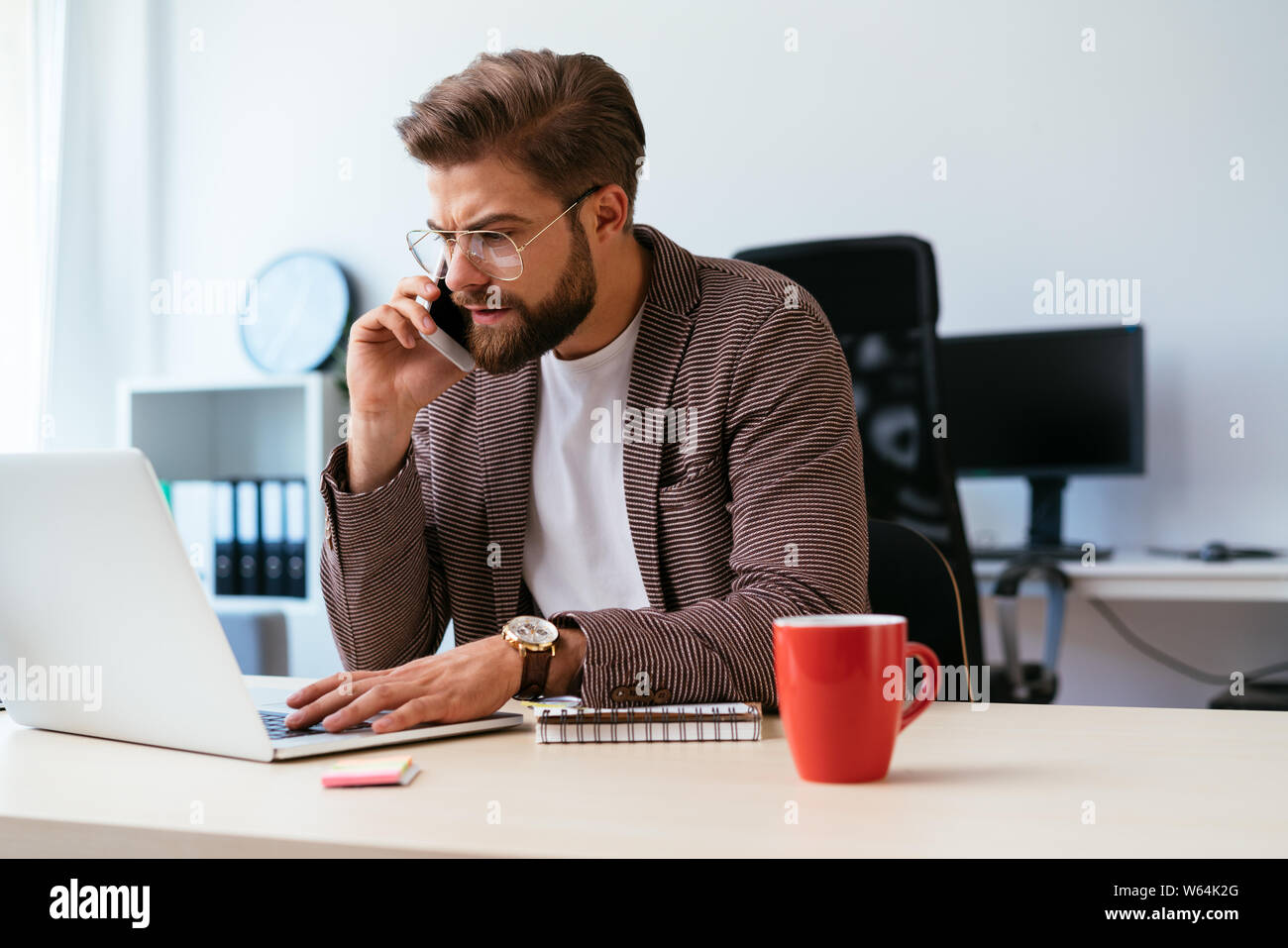 Junge Unternehmer am Telefon sprechen während der Arbeit mit dem Laptop im Home Office Stockfoto