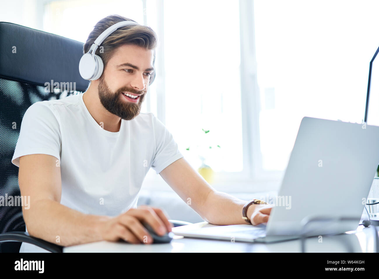 Mann bei der Arbeit auf dem Laptop mit Kopfhörern von Home Office. Studentische Arbeiten am Laptop von einem Zimmer in einem Studentenwohnheim Stockfoto