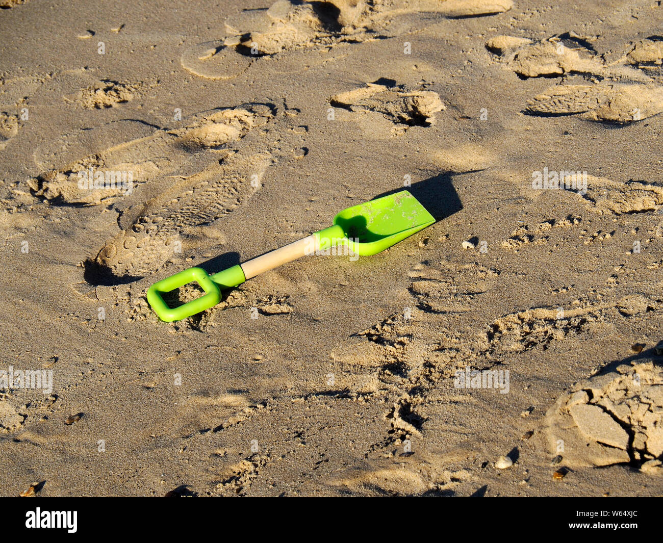 Kunststoff ist ein Kind Spaten liegt an der gelben Sand eines Norfolk Strand aufgegeben das Hinzufügen der Kunststoffe die Verschmutzung unserer Meere. Stockfoto