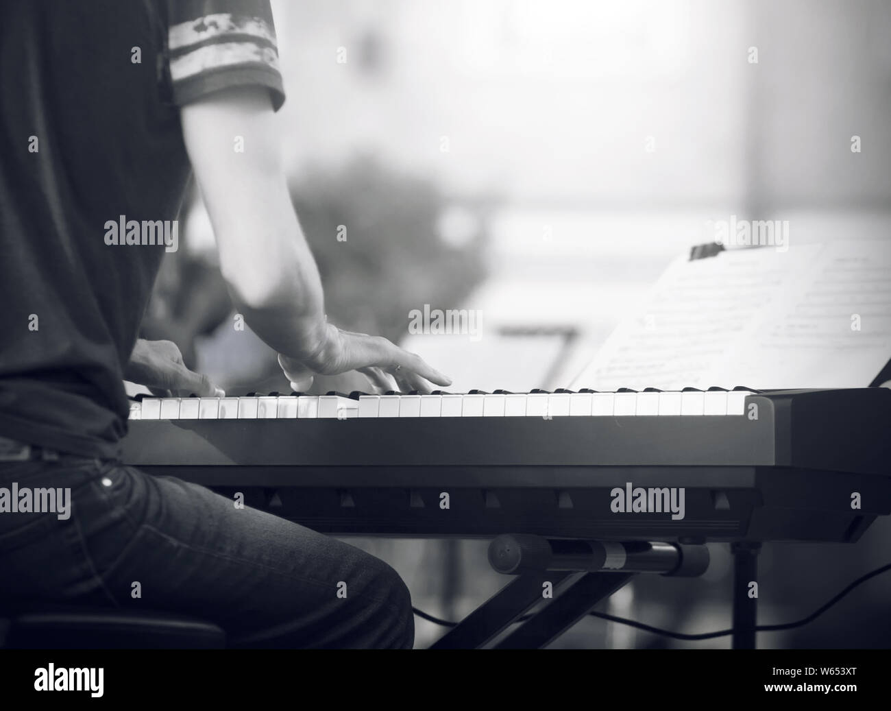 Schwarz-weiß-Bild, wo ein erfahrener Pianist, in einem T-Shirt und Jeans gekleidet, eine schöne Melodie auf dem Synthesizer spielt bei einem Konzert Stockfoto