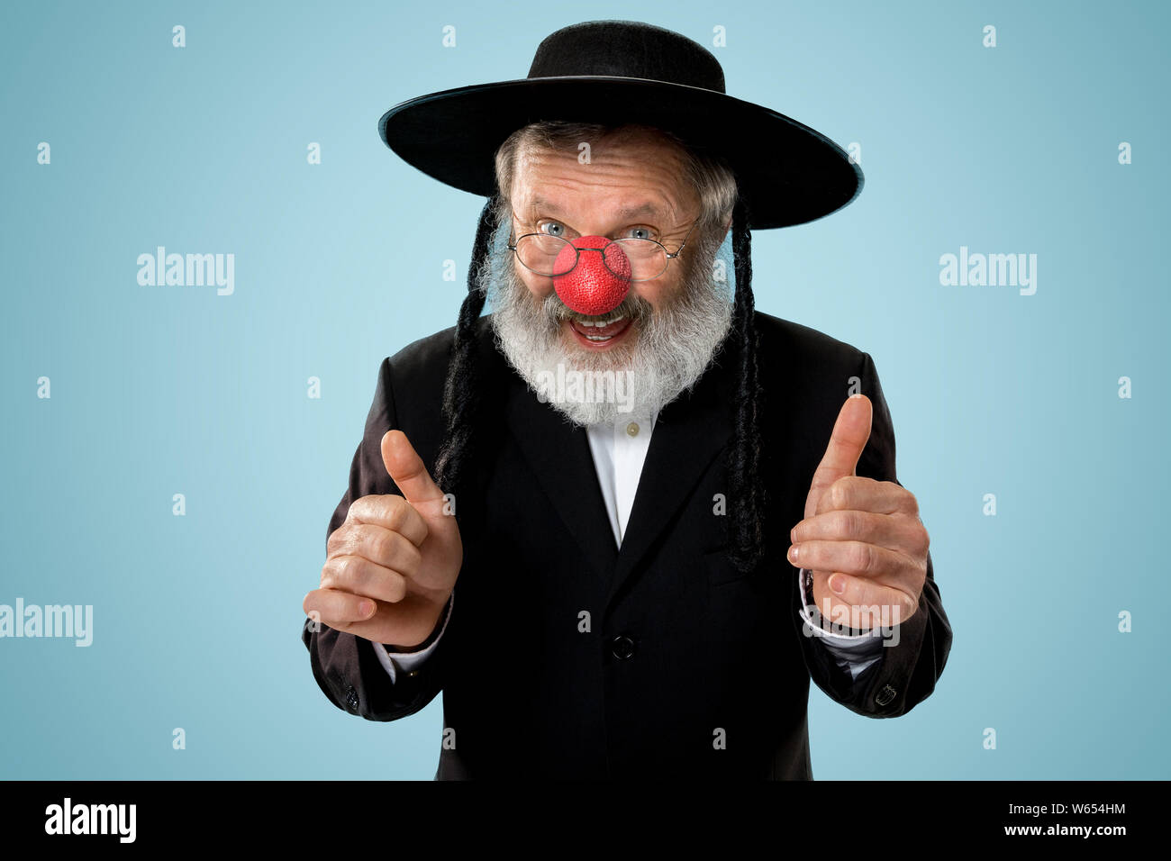 Portrait eines älteren jüdischen Mann feiert red nose day. Purim, Festival, Urlaub, Feier, Judentum, Religion, menschliche Emotionen Konzept. Alter Mann lächelnd auf Blau studio Hintergrund. Stockfoto