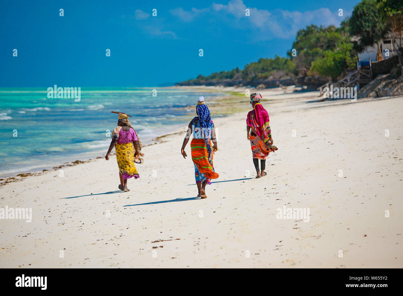 Zanzibar Beach lokale Frauen in helle Kleidung Wandern entlang der Küste Stockfoto