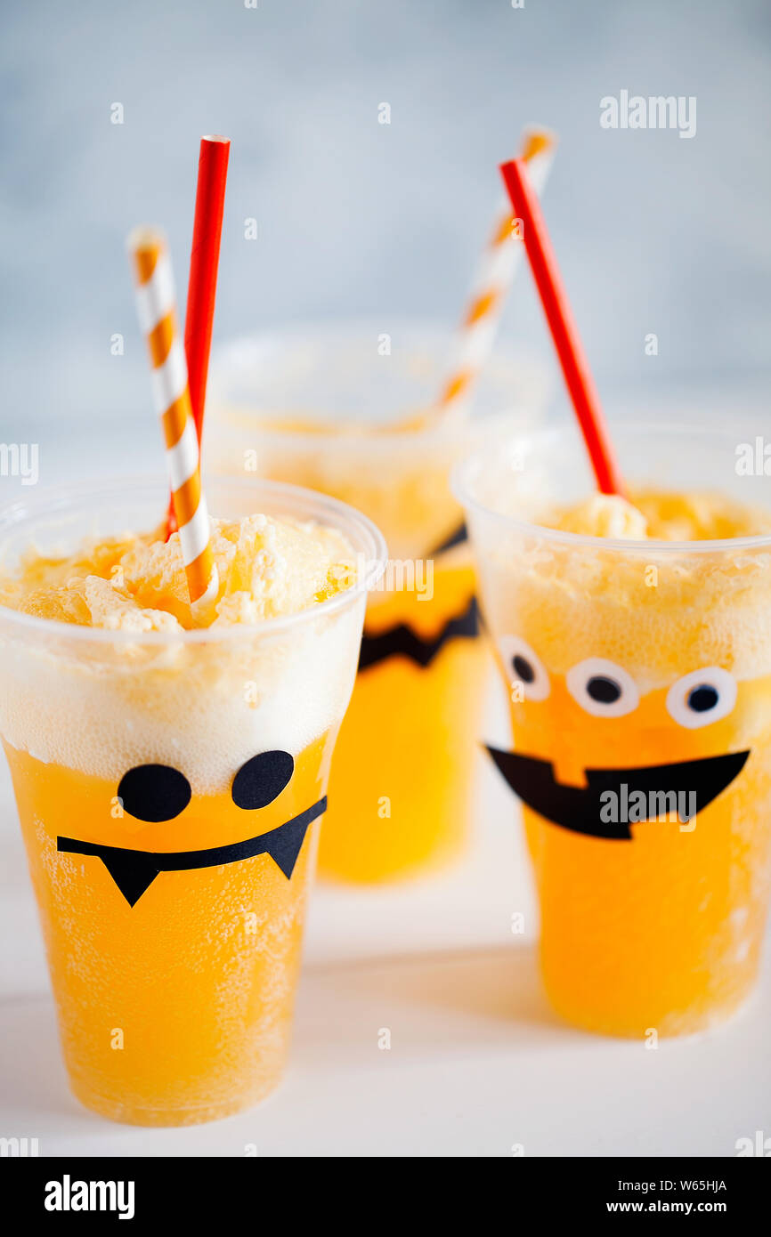 Dekorierte Gläser mit kalten Kürbis orange Cocktail (Punch, Limonade, Schütteln, Smoothie) mit netten, lustigen und gruseligen Gesicht und Sahne für Halloween Stockfoto