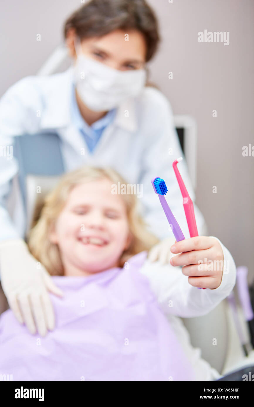 Kind als Patient beim Zahnarzt hält Zahnbürsten als Symbol für gesunde Zahnpflege und Vorsorge Stockfoto