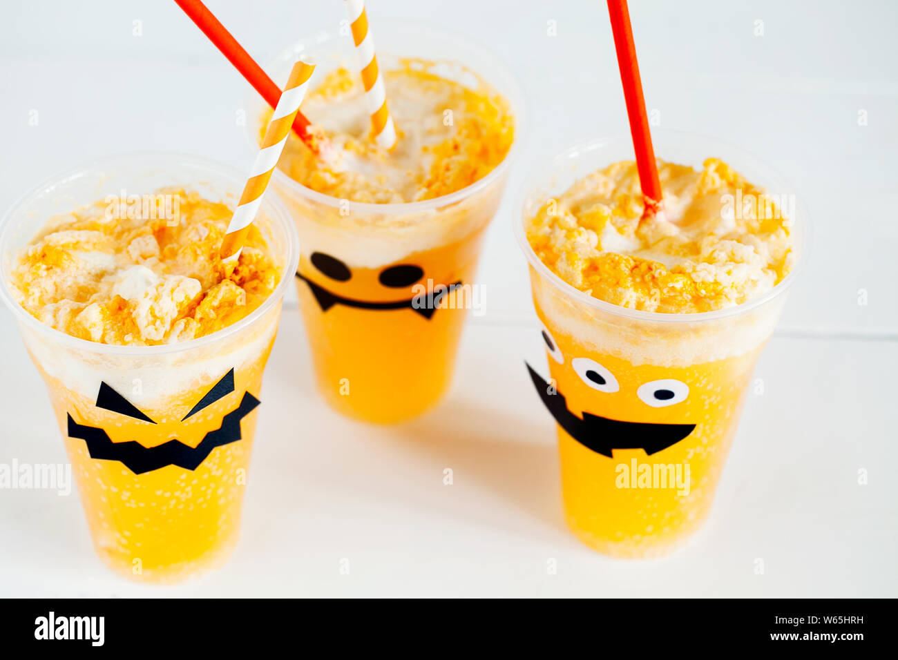 Dekorierte Gläser mit kalten Kürbis orange Cocktail (Punch, Limonade, Schütteln, Smoothie) mit netten, lustigen und gruseligen Gesicht und Sahne für Halloween Stockfoto