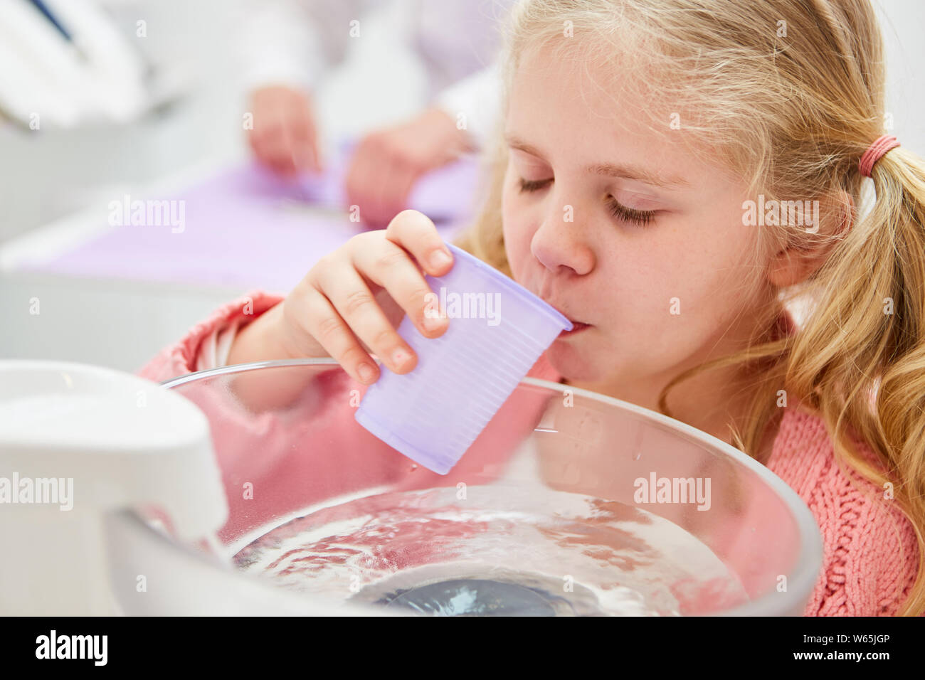 Kleines Mädchen als Patient spült den Mund mit Wasser, während vom Zahnarzt behandelt werden Stockfoto