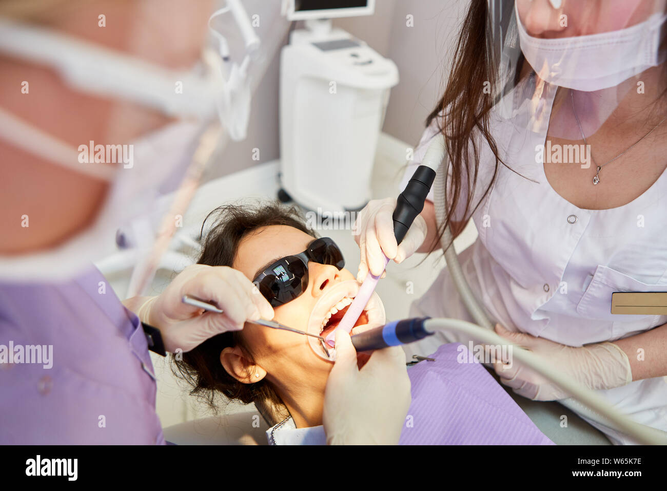 Zahnarzt mit Bohrer und sein Team bei einer Wurzelbehandlung bei einem Patienten Stockfoto