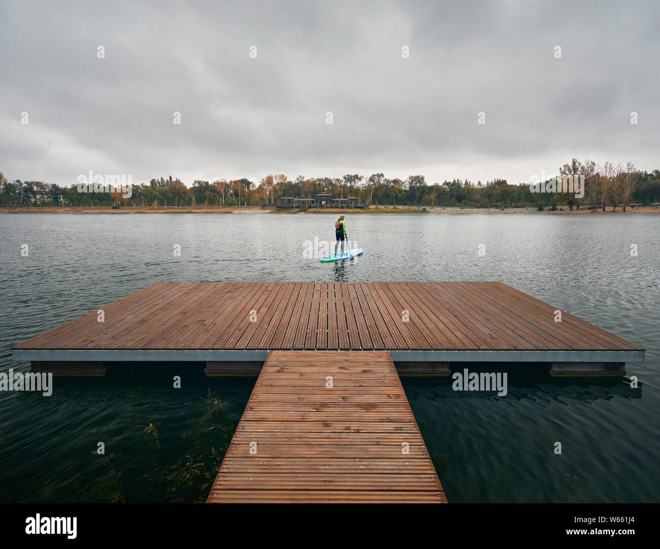 Athlet im Neoprenanzug auf paddleboard Erkundung der See bei kaltem Wetter gegen bewölkten Himmel Stockfoto