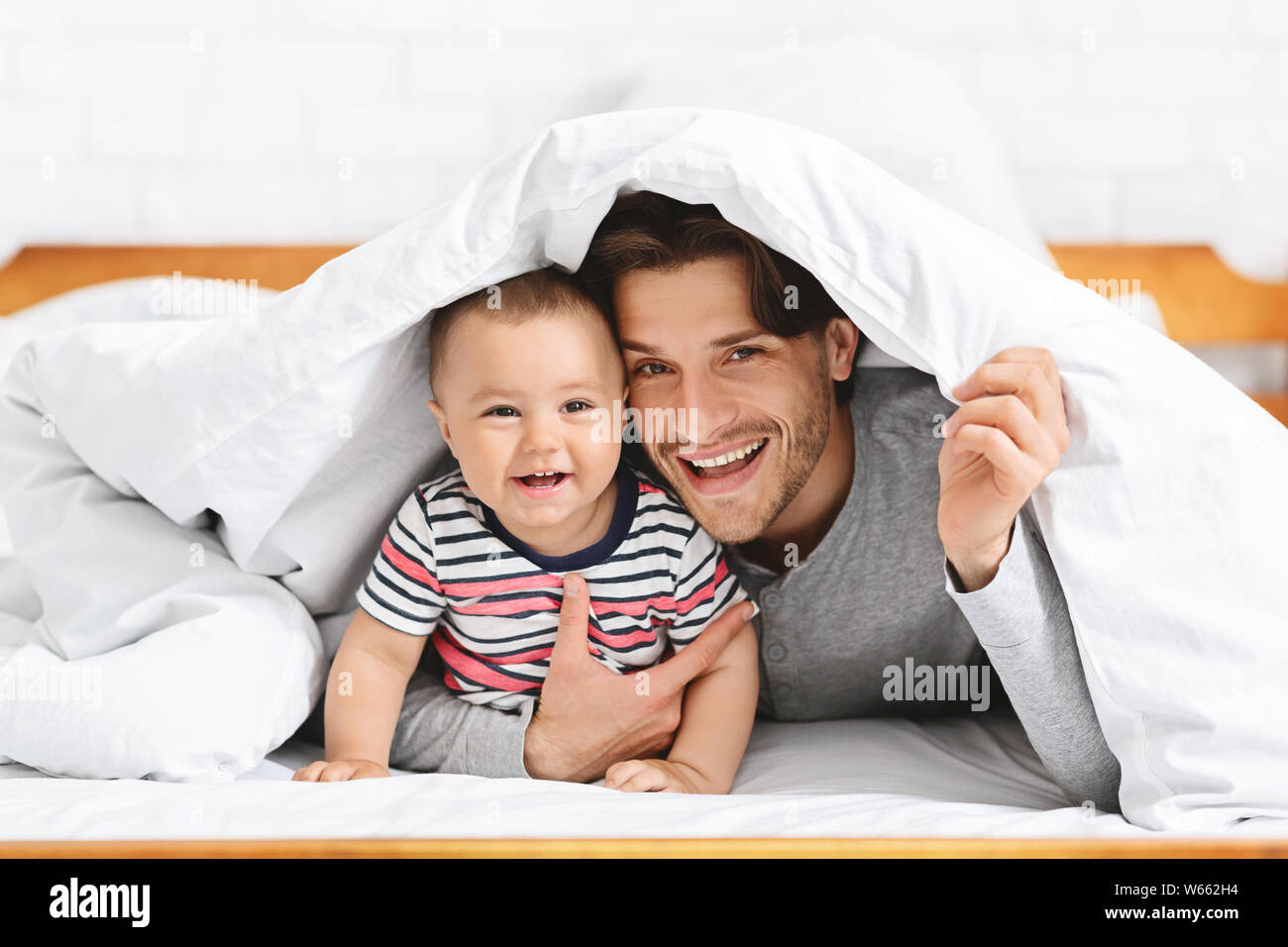 Fröhliches baby versteckt unter Decke mit Vater Stockfoto