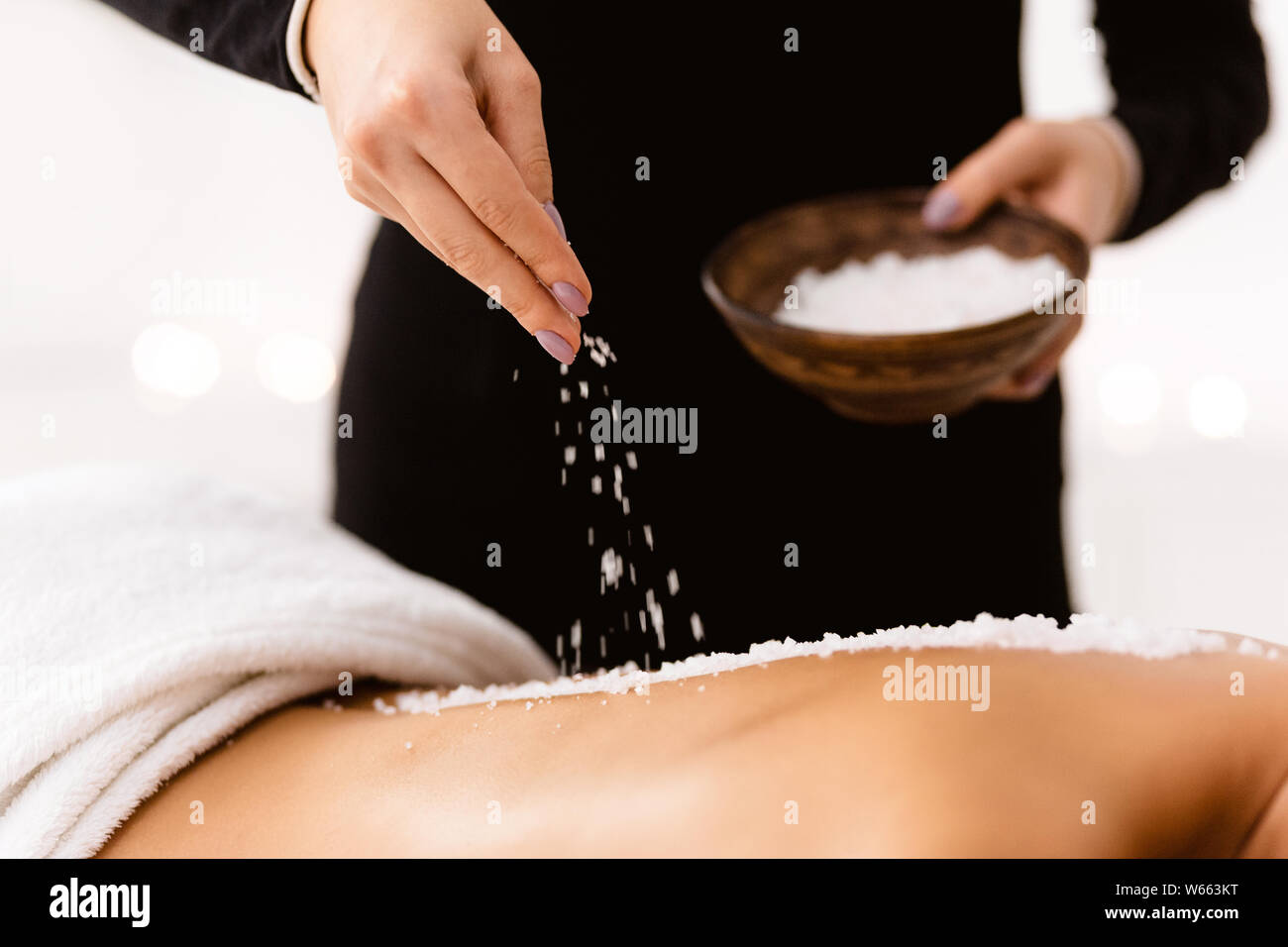 Kosmetikerin gießen Salt Scrub auf Frau zurück an Health Spa Stockfoto