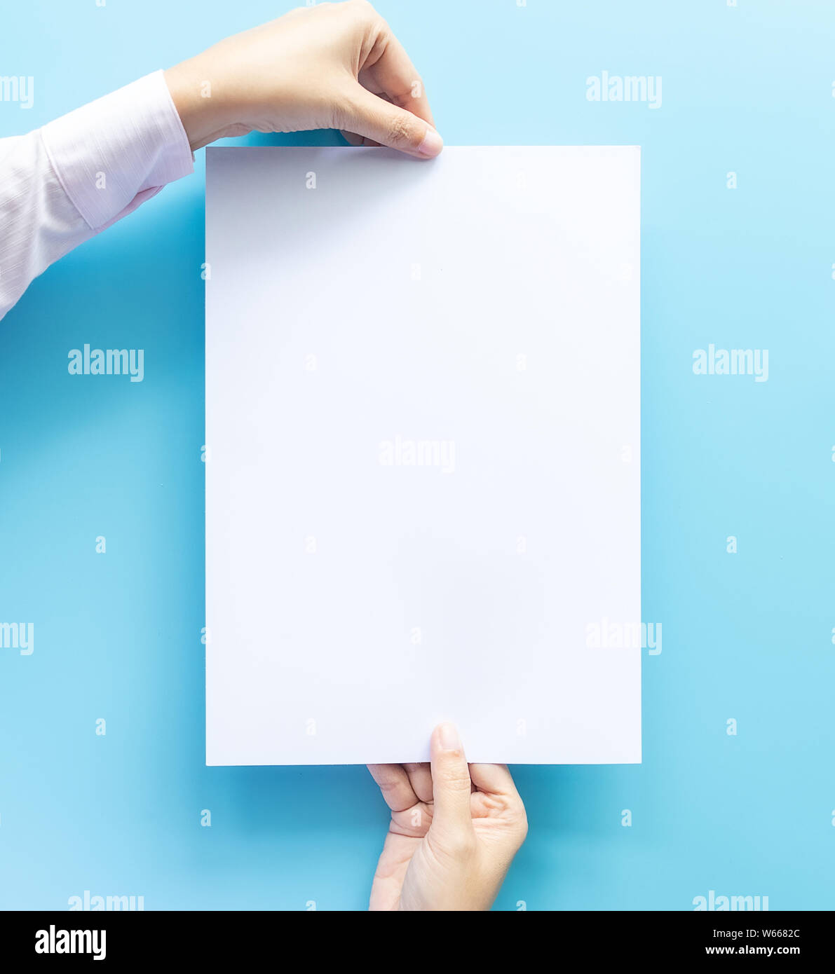 Nahaufnahme der beiden Hände, die leere weiße Leere schreiben Papierformat A4 mit Kopie Platz für Flyer oder Einladung mock up auf einem blauen Hintergrund. Stockfoto