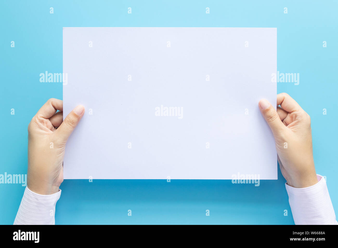 Die Hände schließen Holding leere weiße Leere schreiben Papierformat A4 für Flyer oder Einladung mock up auf einem blauen Hintergrund. Stockfoto