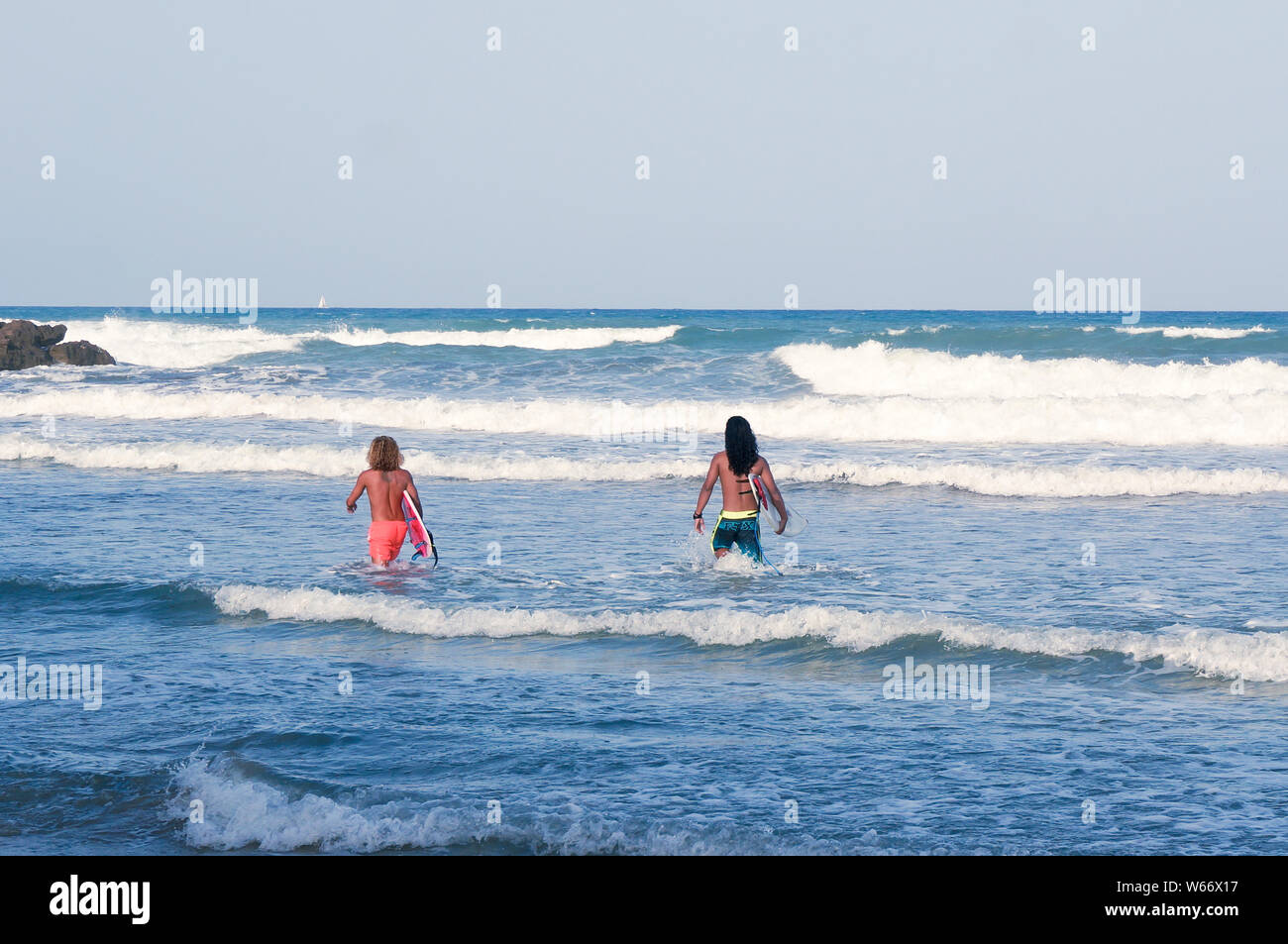 Orihuela Costa, Alicante, Spanien - Juli 2019: Zwei passen junge lange Haare Männer in zum Meer holding Surfen boards laufen Stockfoto