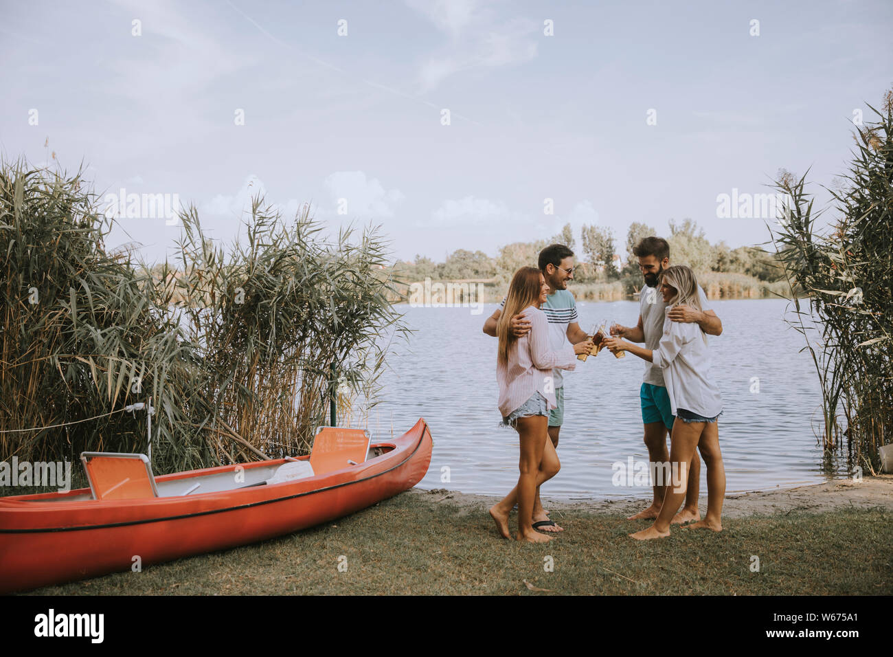 Eine Gruppe von Freunden mit Cider Flaschen stehend durch die Yacht in der Nähe des wunderschönen Sees und Spaß im Sommer Stockfoto