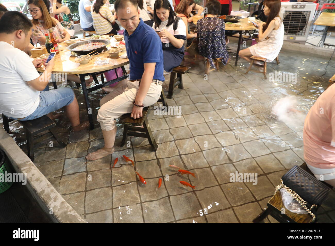 Kunden spielen mit Wasser ihre Füße zu kühlen, wie Sie würziger Eintopf in einem Restaurant in Chongqing, China, 11. Juli 2018 Essen. Zu gewinnen Menschen zu sp Essen Stockfoto