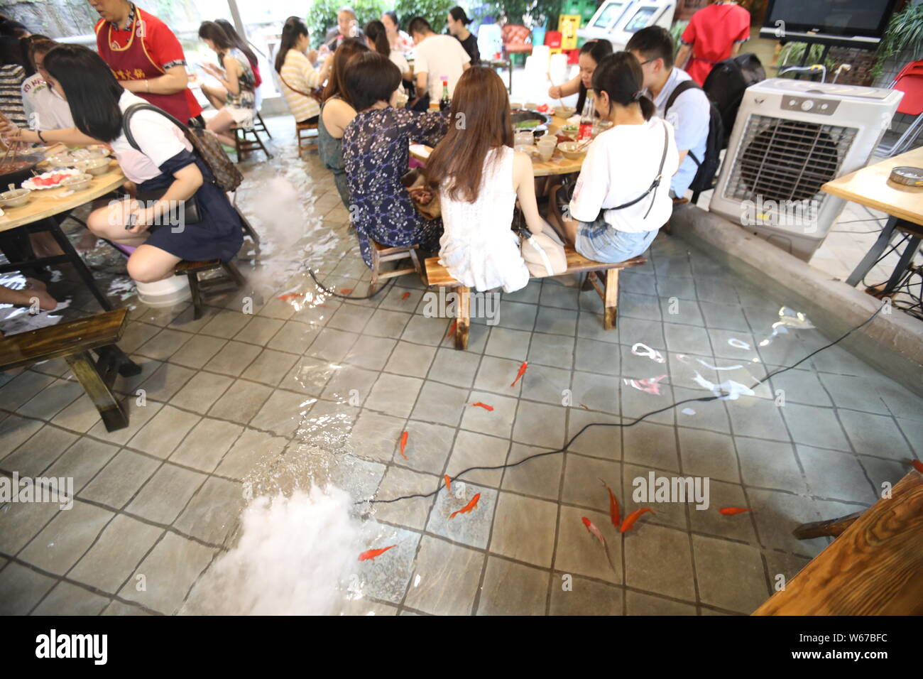 Kunden spielen mit Wasser ihre Füße zu kühlen, wie Sie würziger Eintopf in einem Restaurant in Chongqing, China, 11. Juli 2018 Essen. Zu gewinnen Menschen zu sp Essen Stockfoto