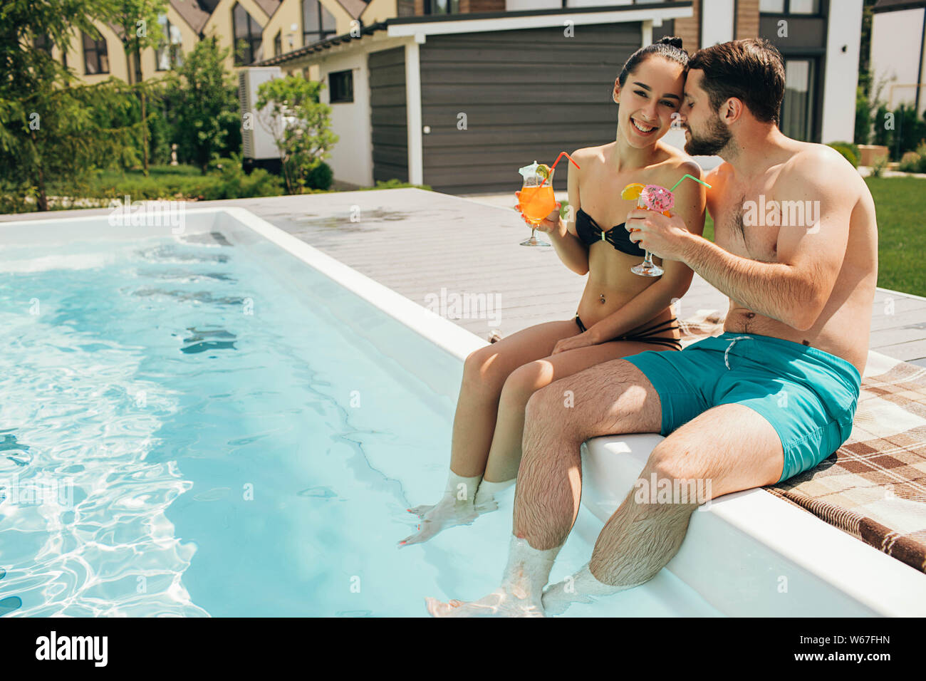 Glückliches Paar Sitzen am Pool im Hinterhof ihres Hauses. Der Mann und die Frau sitzen in der Nähe von Pool und lustig Spritzwasser ihre Beine Stockfoto