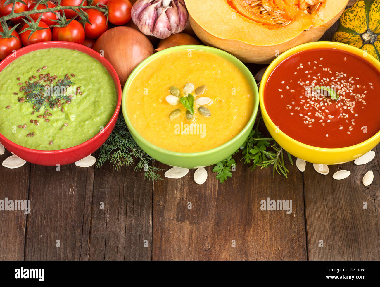 Drei frische Suppen in bunten Schalen und Gemüse auf einem Holztisch Stockfoto