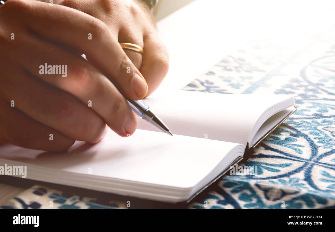 Männliche Hände halten ein Kugelschreiber auf die leeren Seiten eines offenen Notebook zu schreiben. Kreative Moment. Inspiration. Stockfoto