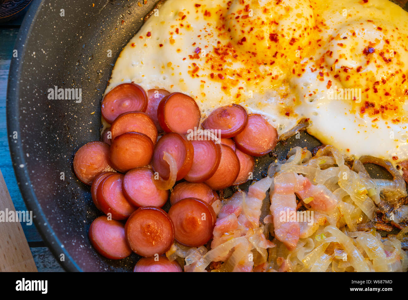 Rührei mit Speck, Zwiebeln und Würstchen. In der Pfanne auf den Tisch. Stockfoto