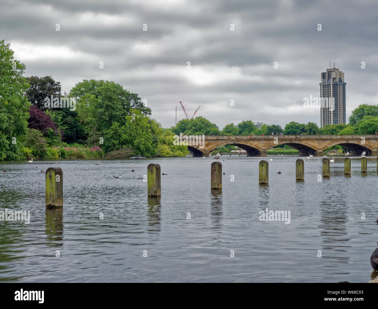 Die lange Wasser in Kensington Gardens, einer städtischen Grünfläche in London, die zu den Sepentine Bridge und die Skyline der Stadt in der Ferne Stockfoto