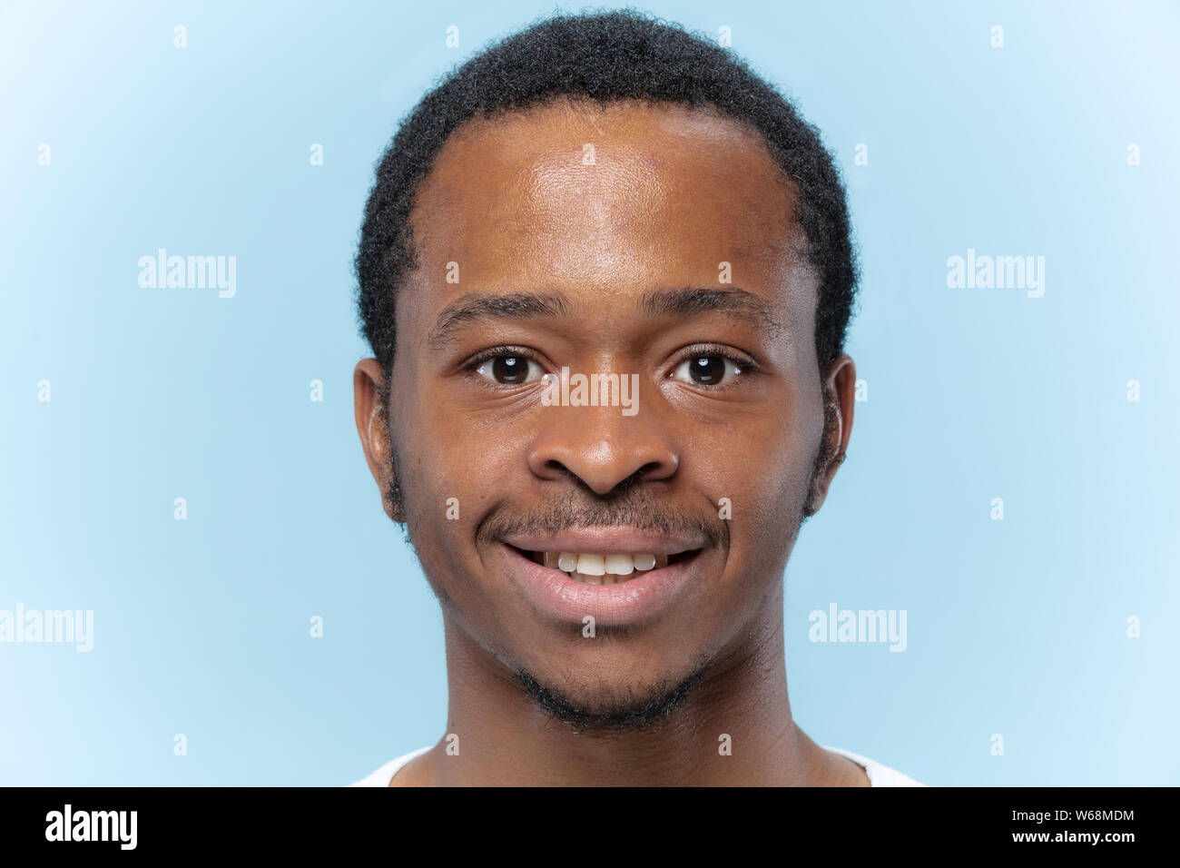 Close up Portrait von jungen afrikanischen - amerikanische Mann im weißen Hemd auf blauem Hintergrund. Menschliche Gefühle, Mimik, ad, Vertriebskonzept. Sieht glücklich lächelnd, an der Kamera schaut. Angenehmes Gefühl. Stockfoto