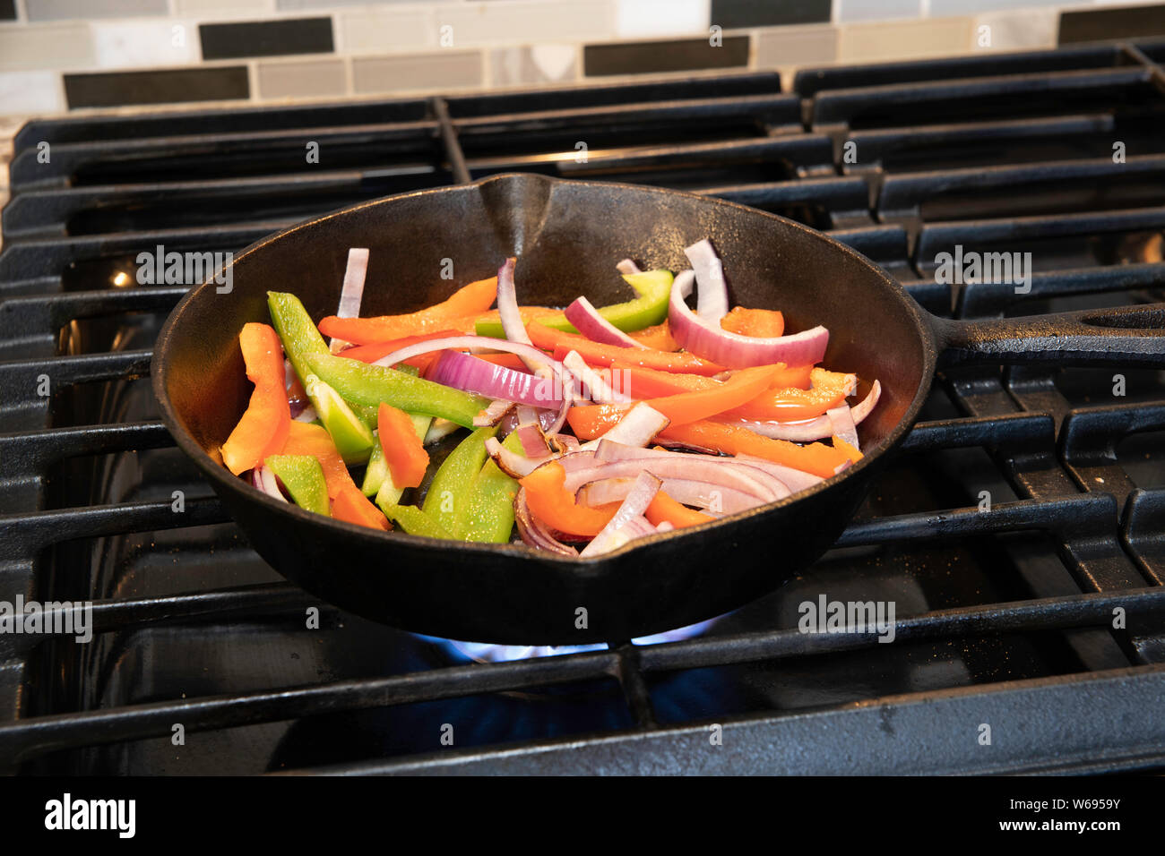 Grüne und rote Paprika und Zwiebeln Grillen in einer gusseisernen Pfanne in Scheiben geschnitten Stockfoto