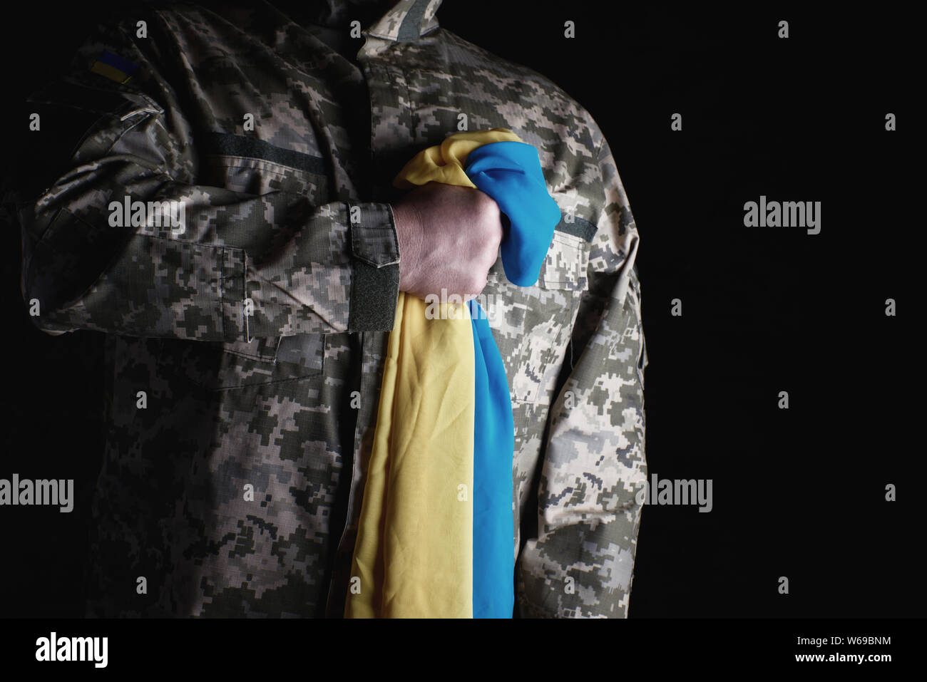 Ukrainische Soldaten hält in seiner Hand das gelb-blaue Flagge des Staates, er presste seine Hand an seine Brust, Konzept der Erinnerung an die toten Soldaten Stockfoto