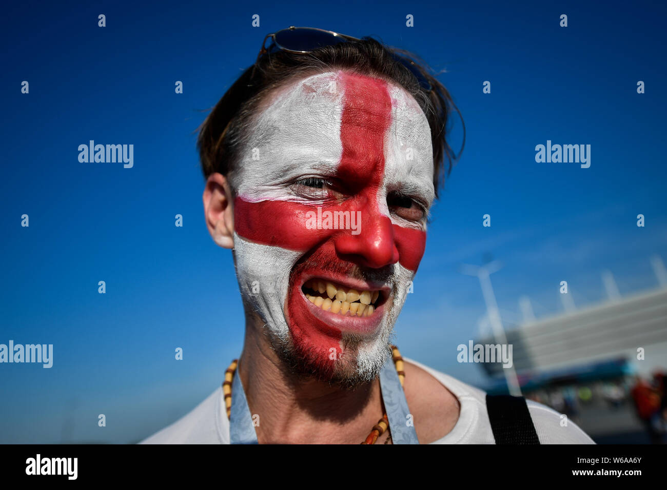 Eine englische Lüfter ist mit einem nationalen Flagge auf seinem Gesicht, als er und andere Sammeln außerhalb der Kaliningrad Stadium vor der Gruppe G Match zwischen Eng lackiert Stockfoto
