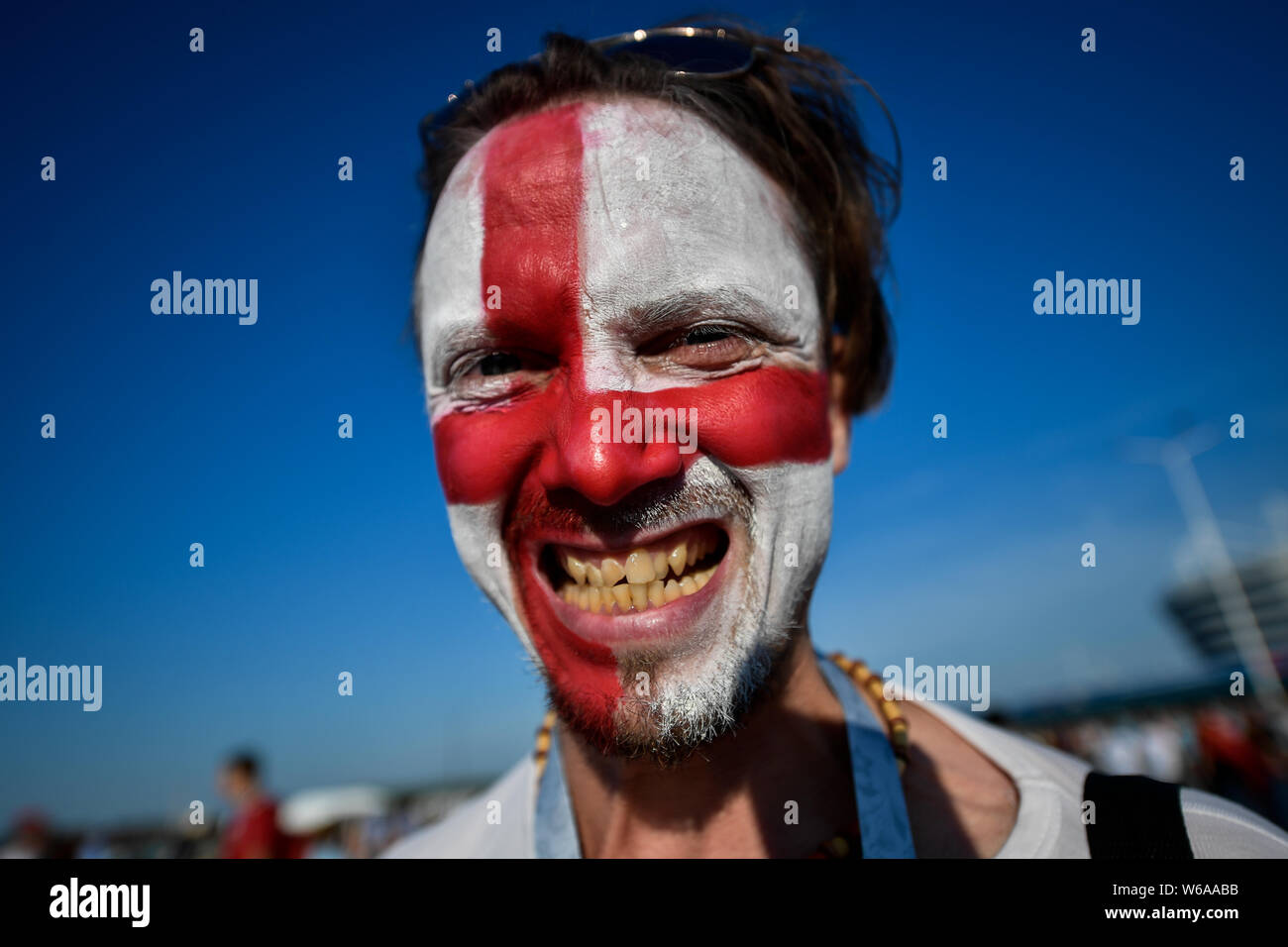Eine englische Lüfter ist mit einem nationalen Flagge auf seinem Gesicht, als er und andere Sammeln außerhalb der Kaliningrad Stadium vor der Gruppe G Match zwischen Eng lackiert Stockfoto