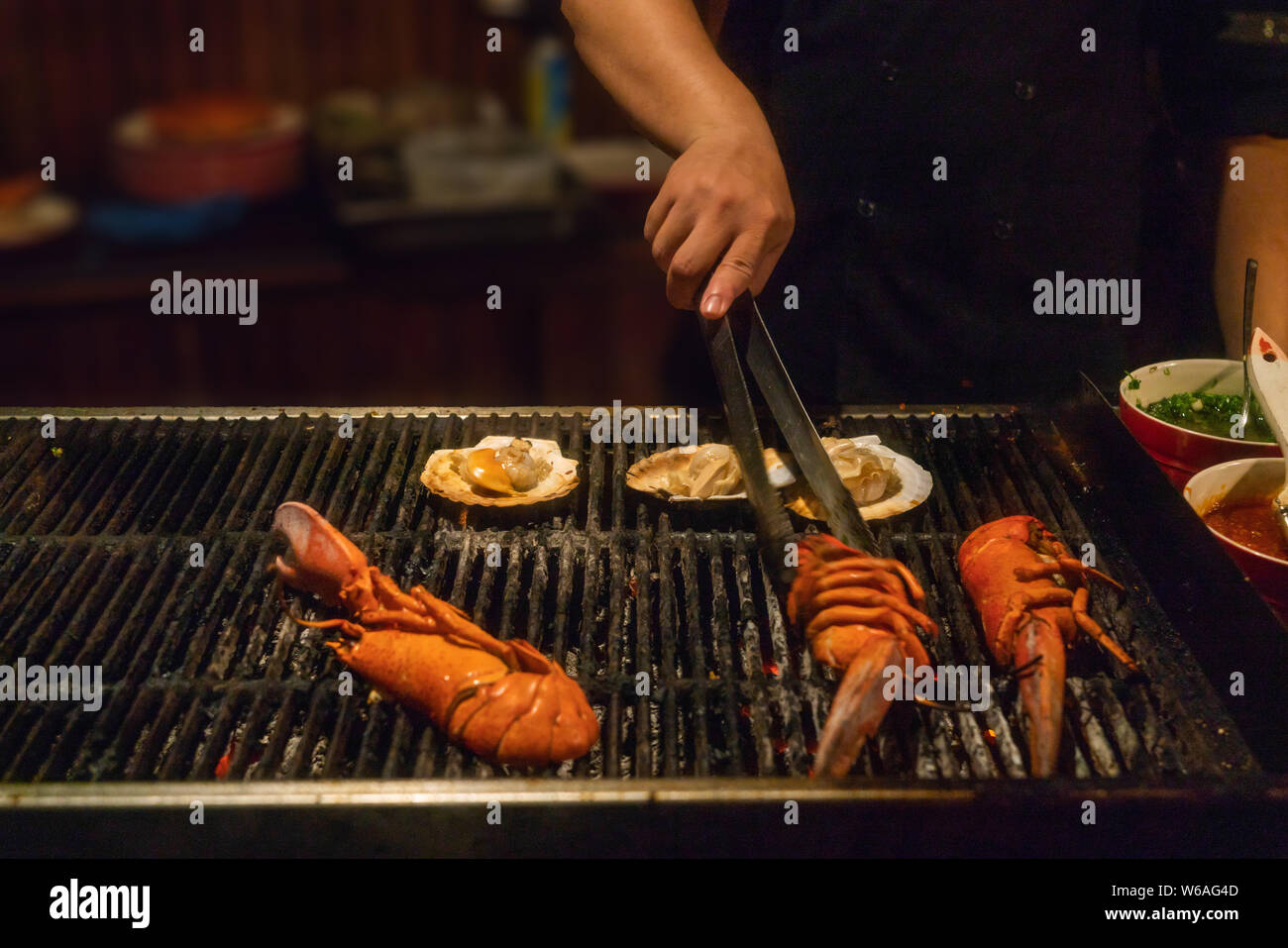 Nahaufnahme einer Hand, die Zangen und grillen Hummer Stockfoto