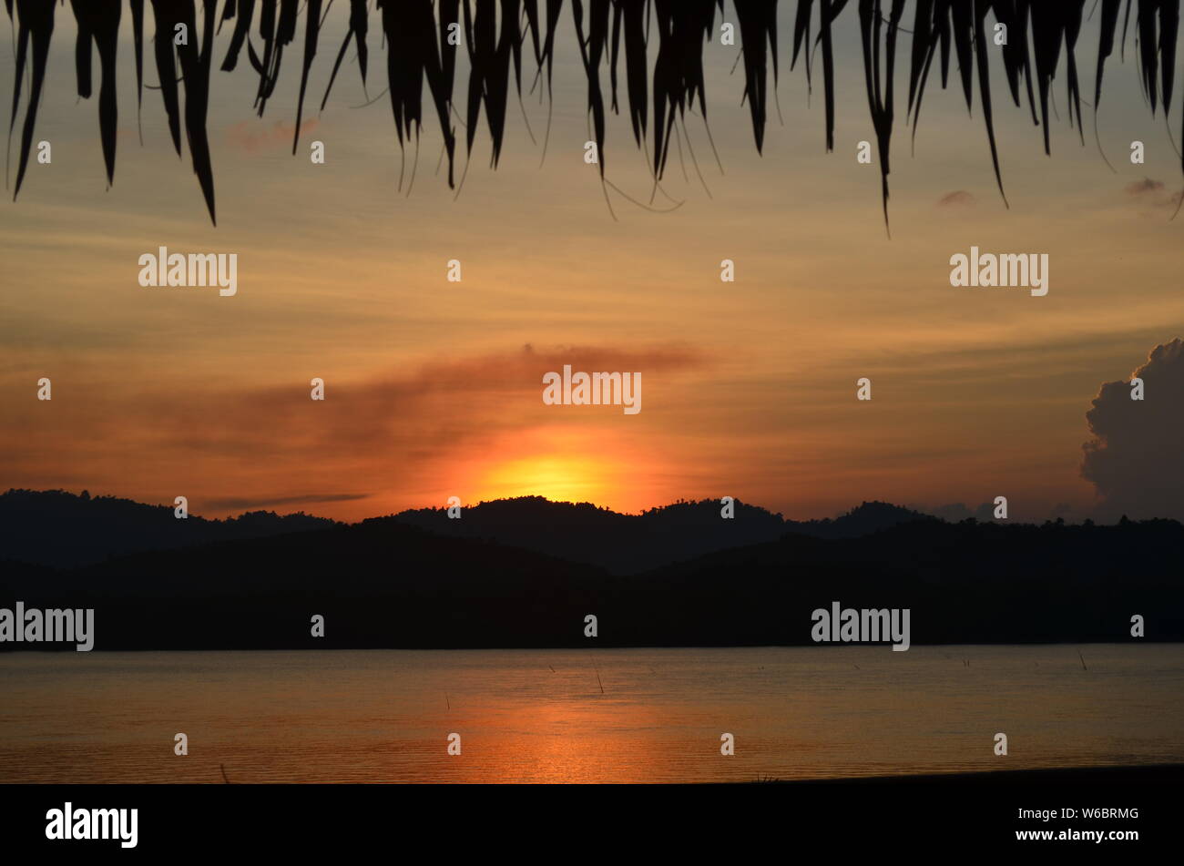 Die Sonne über dem Kra Buri Fluss in Thailand mit Blick auf die Landschaft von Myanmar. Palmwedel fransen oben im Bild Stockfoto