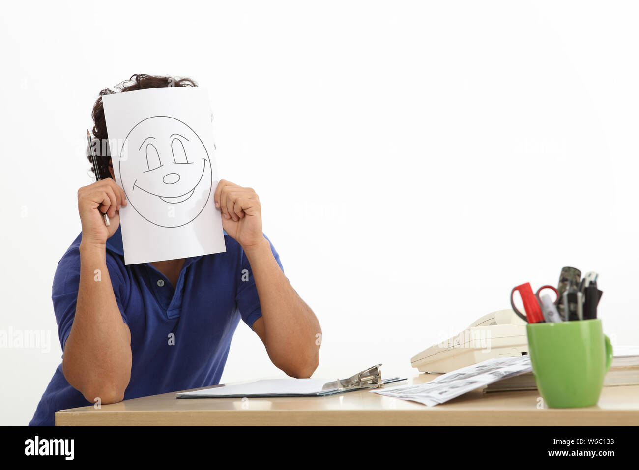 Der Modedesigner hält ein Smiley-Gesicht auf dem Blatt Papier über seinem Gesicht Stockfoto