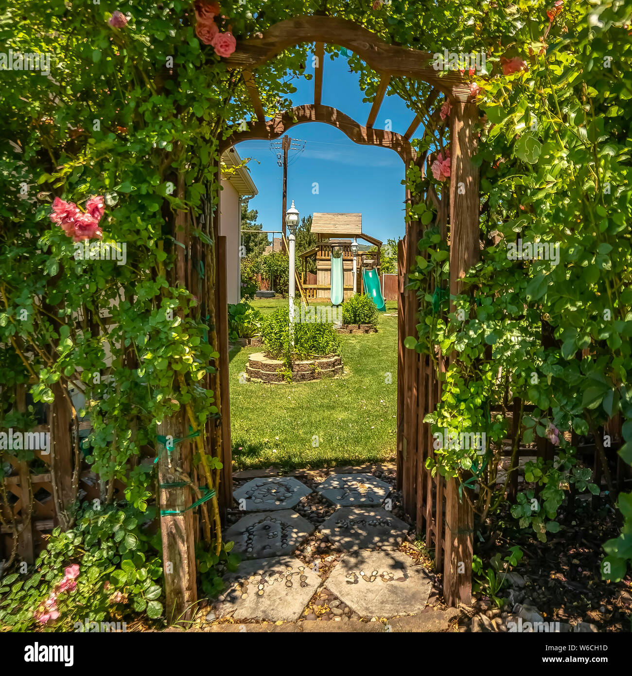 Quadrat gewölbt Holz- Arbor am Eingang eines Garten mit Spielhaus Rutsche und Schaukeln Stockfoto